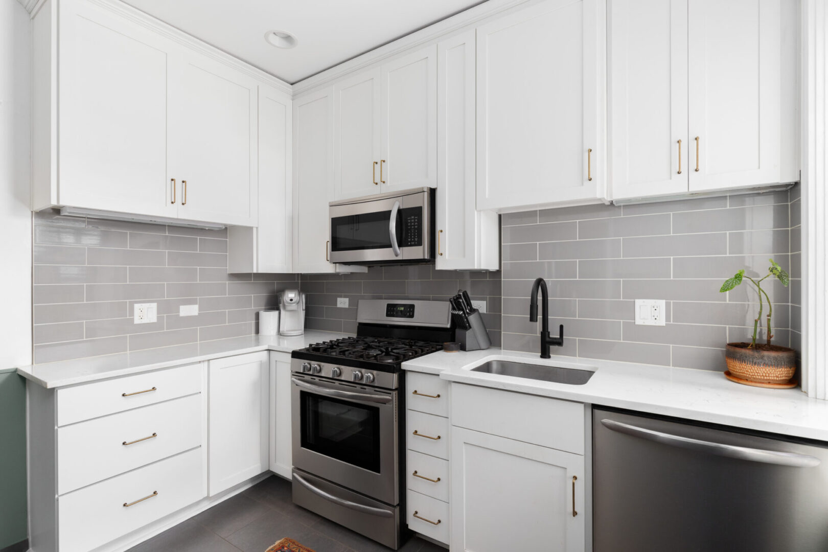 A kitchen with white cabinets and gray tile.